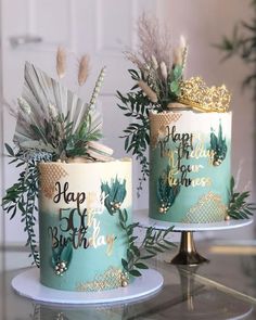 two birthday cakes decorated with plants on top of a cake stand, one is blue and the other has gold lettering