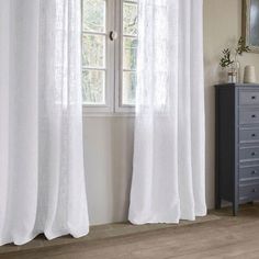 a white curtain hanging on the side of a window next to a dresser and mirror