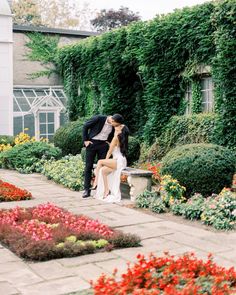 a bride and groom kissing on a bench in front of a garden filled with flowers