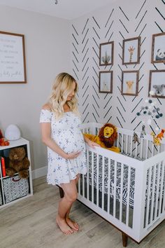 a woman standing next to a baby crib in a room with pictures on the wall