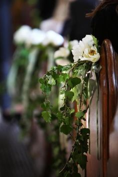 white flowers and greenery on the back of a wooden church pew, with people in the background