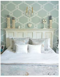 a white bed topped with lots of pillows next to a wallpapered headboard