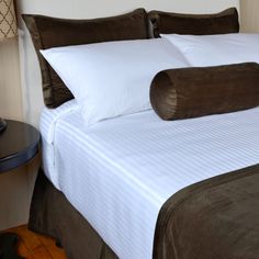 a bed with white and brown pillows on top of it next to a night stand