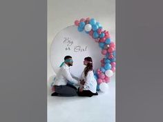 a man and woman sitting in front of a balloon arch