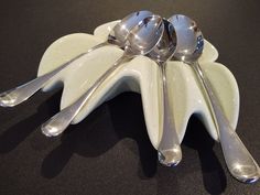 three spoons are sitting on top of a white flower shaped dish with silver handles