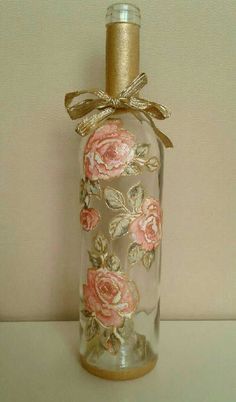 a glass bottle with pink roses and gold ribbon tied around the top is sitting on a table