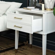 a white table with two drawers and a phone on it in front of a bed