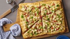 a pizza with many toppings on a cutting board next to a knife and fork