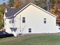 a white house sitting on top of a lush green field next to a black car