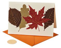 a card with leaves on it and an orange envelope next to the card is a penny