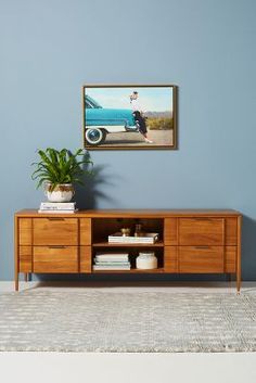 a room with a blue wall and a painting on the wall above a wooden cabinet