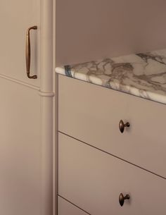 a marble counter top in front of a white cabinet with brass handles and knobs