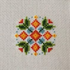 a cross stitch pattern on a piece of white fabric with orange, blue and green flowers