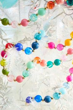 colorful beads are hanging from a glass tree ornament on a white christmas tree