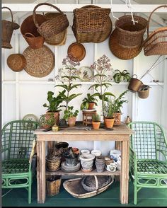 several baskets hanging from the ceiling above a table with plants on it and two green chairs