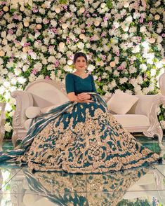 a woman in a blue and gold dress sitting on a couch with flowers behind her