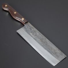 a large knife with a wooden handle on a black tableclothed surface and gold dots around the blade