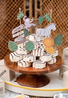 desserts are arranged on a wooden platter at a safari themed birthday party, including zebra and giraffe cupcakes