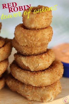 a stack of fried onion rings sitting on top of a wooden cutting board next to a blue bowl