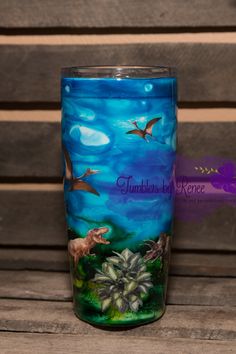 a blue glass with dinosaurs on it sitting on a wooden table next to a bench