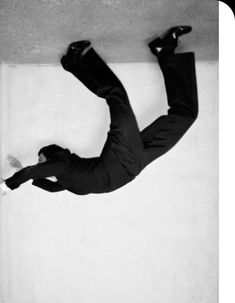 black and white photograph of a man falling off the side of a building with his feet in the air