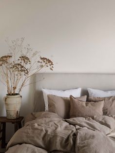 an unmade bed with white sheets and pillows in a small room next to a plant