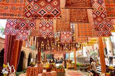 an outdoor area with many different colored rugs hanging from the ceiling and tables set up in front of them