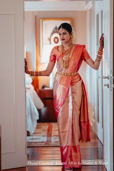 a woman in an orange and pink sari walking into a room with her hand on the door