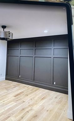 an empty room with wood flooring and black cabinetry on the wall, in front of a flat screen tv