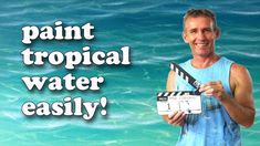 a man holding a clapstick in front of the ocean with words paint tropical water easily