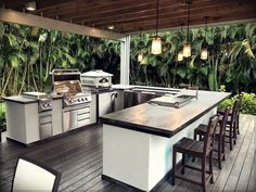 an outdoor kitchen with grill and bar stools on the deck area, surrounded by palm trees