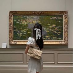 a woman holding a purse looking at a painting in a museum with water lillies