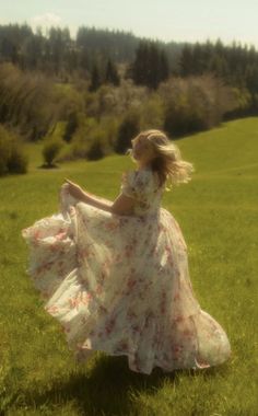 a woman in a long dress is walking through the grass with her arms spread out