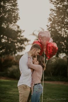 a man and woman standing next to each other with red balloons in the shape of hearts