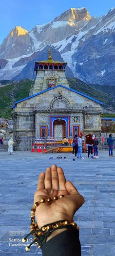 a person holding their hand up in front of a building with mountains in the background