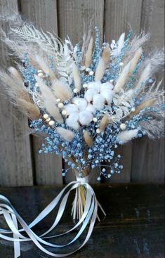 a vase filled with cotton and feathers on top of a wooden table next to a white ribbon