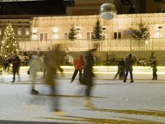 people skating on an ice rink at night with christmas lights in the building behind them