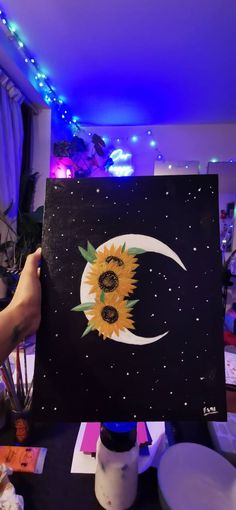 a person holding up a sunflower painting in front of a purple background with blue lights