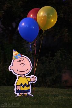 a charlie brown birthday card with balloons and a party hat in the grass at night