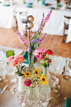 an arrangement of flowers in vases on a table with place settings and napkins