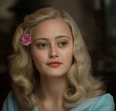 a woman with blonde hair and a pink flower in her hair is looking at the camera