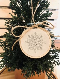 a cross stitch ornament hanging from a potted plant on a wooden table