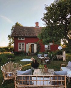 a wooden table sitting in front of a red house with lots of furniture around it