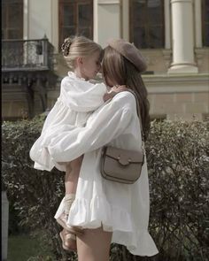 two young women are hugging each other in front of a building with bushes and shrubbery