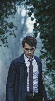 a man wearing a coat and tie standing in the woods