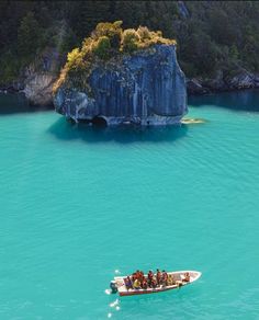 a group of people on a small boat in the water next to a large rock formation