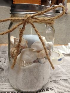 a mason jar filled with seashells and twine on top of a newspaper