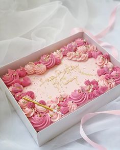 a birthday cake in a box with pink frosting and gold writing on it, sitting on a white tablecloth