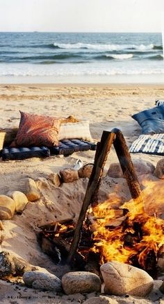 a campfire on the beach with pillows and blankets