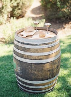 a wooden barrel with two wine glasses on top sitting in the grass next to some rocks